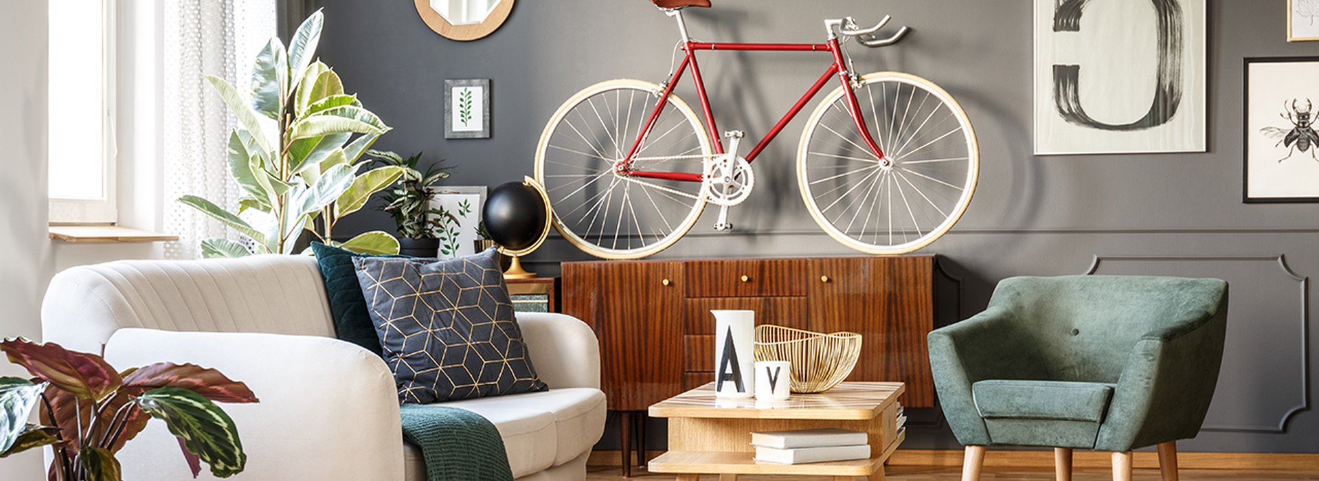 Vintage unique living room interior with good vibes with white comfortable sofa with cushions and blanket and green armchair, cupboard, small table, red bicycle and lots of details including a poster with number five on gray wall